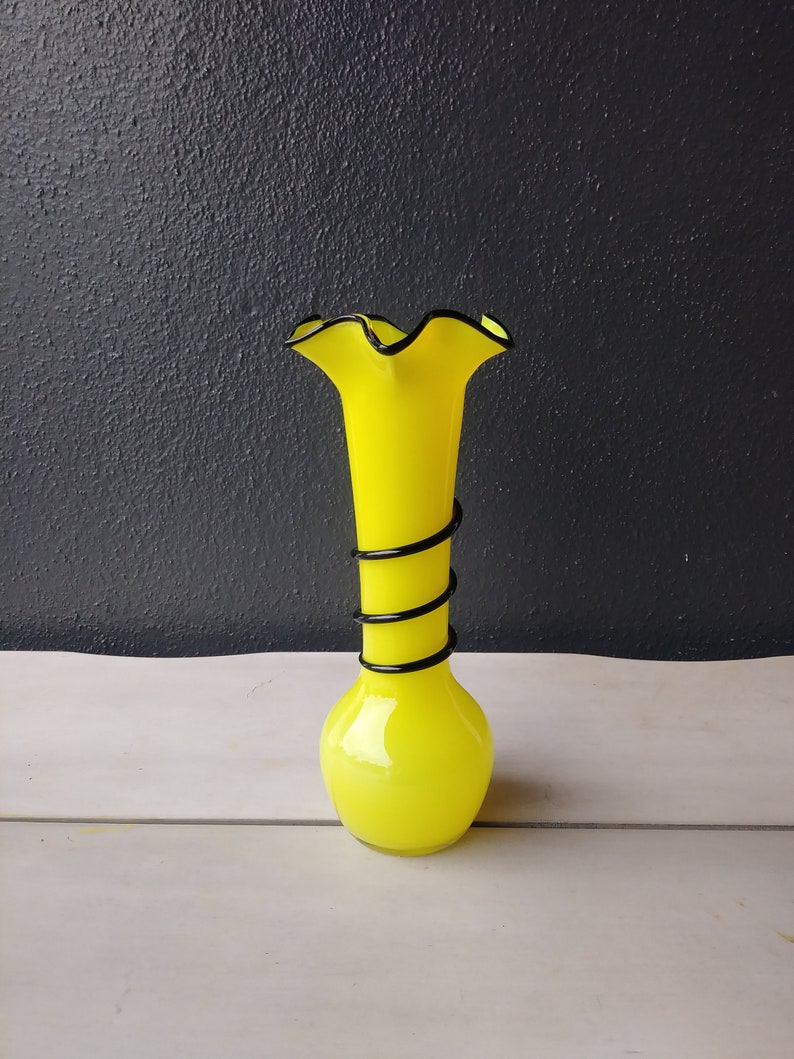 May include: A bright yellow glass vase with a black swirl design and a ruffled top.
