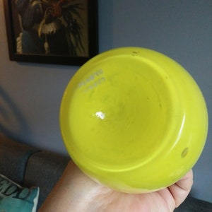 May include: A bright yellow glass vase with a round shape. The vase is empty and has a smooth, glossy finish.