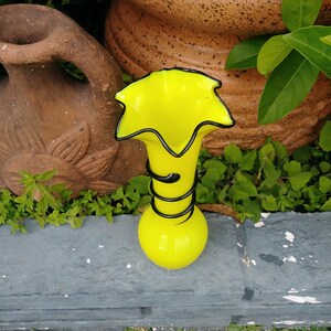 May include: A bright yellow glass vase with a black swirl design. The vase has a wide, flared opening and a narrow base.