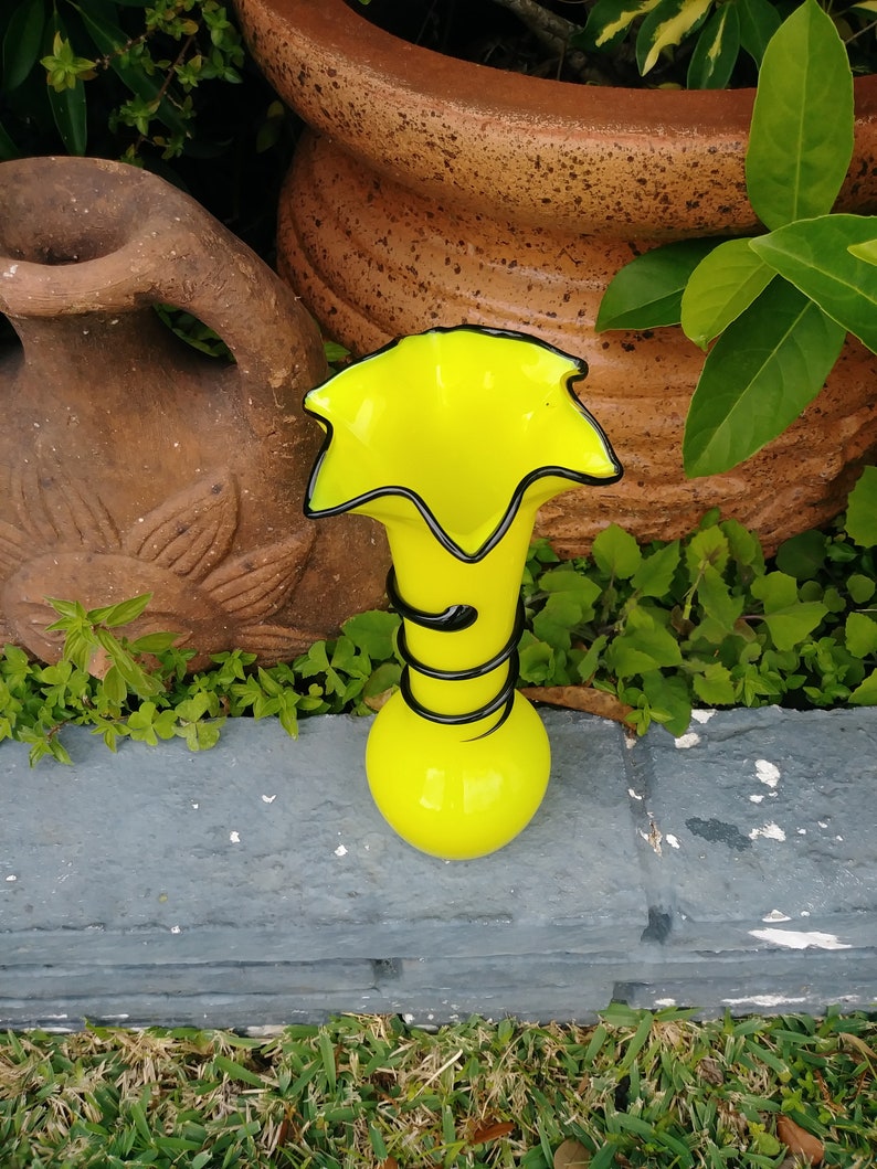 May include: A bright yellow glass vase with a black swirl design. The vase has a wide, flared opening and a narrow base.