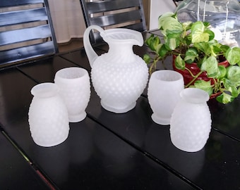May include: Set of five white frosted glass pitcher and glasses with a textured surface. The pitcher has a handle and a rounded body. The glasses are all the same size and shape.