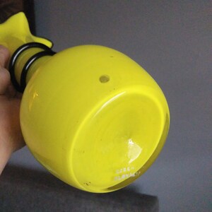 May include: Yellow glass vase with a black metal neck and base. The vase has a round body and a flat bottom. The bottom of the vase is marked with the text "CZECH SLOVAKIA".