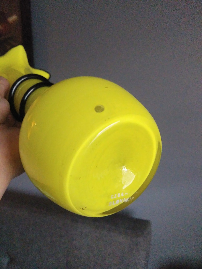 May include: Yellow glass vase with a black metal neck and base. The vase has a round body and a flat bottom. The bottom of the vase is marked with the text "CZECH SLOVAKIA".