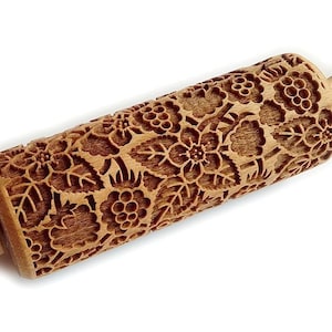 May include: A wooden rolling pin with a detailed floral design, featuring leaves and berries. The rolling pin is made of natural wood and has a smooth, polished finish.