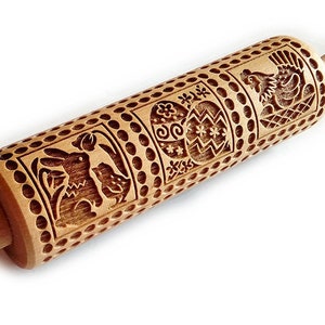 Pode incluir: Rolo de massa de madeira com um design entalhado de um coelho da Páscoa, um ovo e uma galinha. O rolo é feito de madeira marrom claro e tem uma alça em cada extremidade.