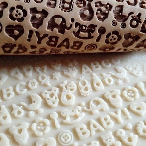 May include: A wooden rolling pin with a baby-themed design, including letters, animals, and other baby-related symbols. The rolling pin is used to create impressions in dough, such as for cookies or fondant.