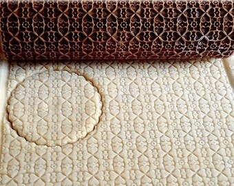 May include: A wooden rolling pin with a detailed carved pattern is used to roll out dough. The dough is imprinted with the pattern from the rolling pin. A round cookie cutter is used to cut out a cookie from the dough.