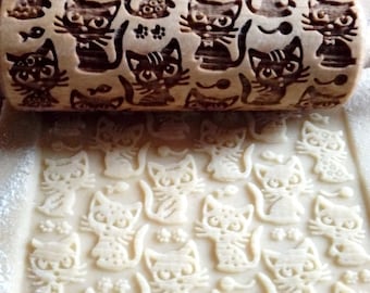 May include: A wooden rolling pin with a carved design of cats and fish. The rolling pin is being used to create an imprint of the design on a sheet of dough.