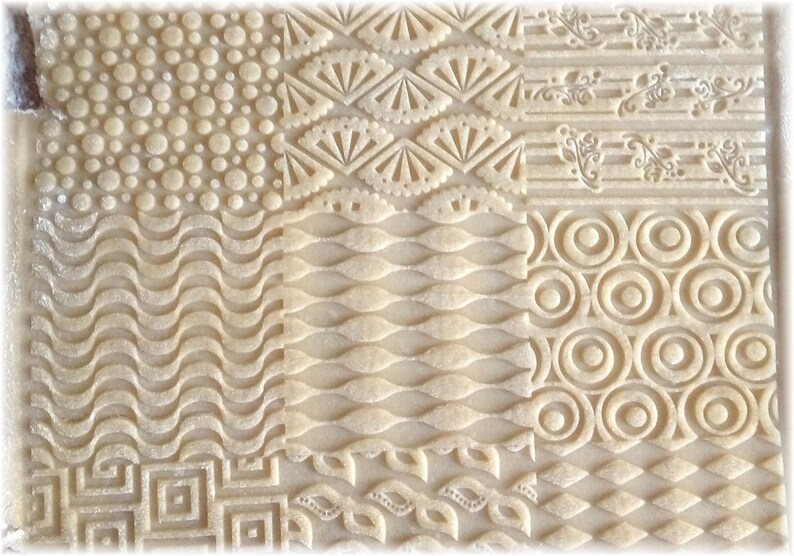 May include: A close-up of a sheet of dough with various patterns embossed into it. The patterns include circles, waves, leaves, and geometric shapes.