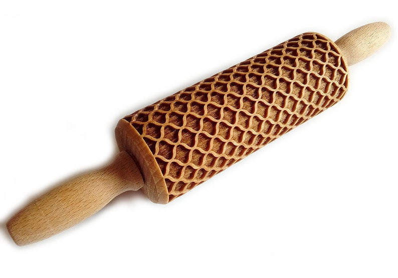 Puede incluir: Un rodillo de madera con un patr&oacute;n decorativo y texturizado. El rodillo tiene un color marr&oacute;n claro y un dise&ntilde;o geom&eacute;trico tallado en la superficie de rodadura. Los mangos son lisos y redondeados. Esta herramienta de cocina est&aacute; dise&ntilde;ada para hornear.