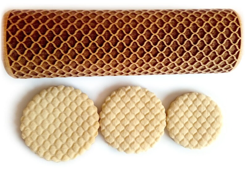 Puede incluir: Un rodillo de madera marr&oacute;n claro con un dise&ntilde;o de celos&iacute;a y tres galletas redondas con el mismo patr&oacute;n. El rodillo y las galletas est&aacute;n sobre un fondo blanco. El patr&oacute;n es un dise&ntilde;o de diamantes repetido.