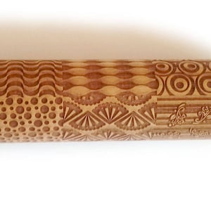 May include: A wooden rolling pin with a variety of engraved patterns, including waves, circles, dots, and a fan design. The rolling pin is brown and has a natural wood finish.