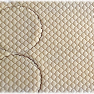 Puede incluir: Primer plano de una l&aacute;mina de masa con un patr&oacute;n de diamantes y dos recortes circulares con bordes festoneados. La masa es de color beige claro y el patr&oacute;n est&aacute; grabado.