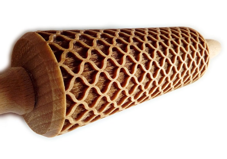 Puede incluir: Un rodillo de madera con un patr&oacute;n de celos&iacute;a decorativo y repetitivo tallado en la superficie de rodadura. Los mangos son lisos y de color claro, mientras que la secci&oacute;n estampada es de un tono marr&oacute;n m&aacute;s oscuro.