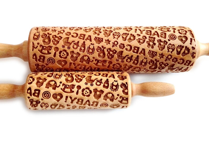 May include: Two wooden rolling pins with a baby theme. The rolling pins are engraved with letters, hearts, stars, and other baby-related designs. The larger rolling pin is 10 inches long and the smaller rolling pin is 6 inches long.