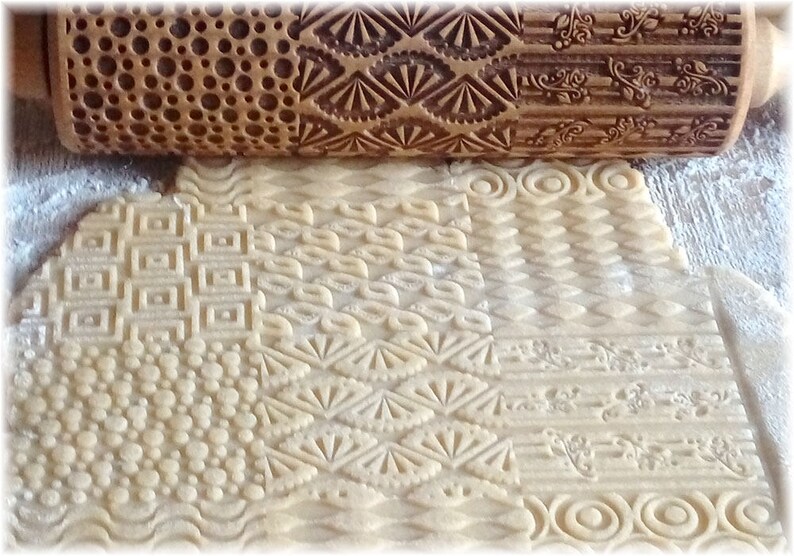 May include: A wooden rolling pin with different engraved patterns is used to create decorative designs on a sheet of dough. The patterns include circles, squares, diamonds, and floral designs.