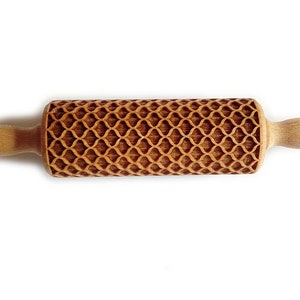 Puede incluir: Un rodillo de madera con un patr&oacute;n decorativo y texturizado. El rodillo tiene un cuerpo cil&iacute;ndrico con un dise&ntilde;o geom&eacute;trico repetitivo y dos mangos de madera. El rodillo est&aacute; hecho de madera de color claro.