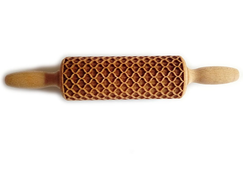 Puede incluir: Un rodillo de madera con un patr&oacute;n decorativo y texturizado. El rodillo tiene un cuerpo cil&iacute;ndrico con un dise&ntilde;o geom&eacute;trico repetitivo y dos mangos de madera. El rodillo est&aacute; hecho de madera de color claro.