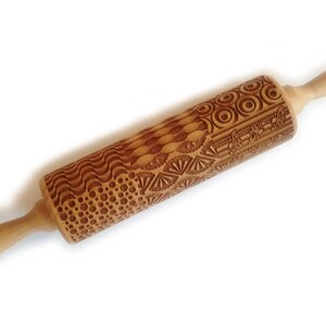 May include: A wooden rolling pin with a decorative engraved pattern of circles, waves, and geometric shapes. The rolling pin is brown and has two wooden handles.