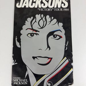 May include: A rectangular poster featuring a stylized graphic illustration of Michael Jackson in black, white, and gray. The text reads THE JACKSONS VICTORY TOUR 1984 and FEATURING MICHAEL JACKSON. The design includes subtle red and blue accents.