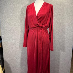 Op de afbeelding: Een rode jurk met lange mouwen, een V-hals en een wikkel-stijl lijfje. De jurk wordt getoond op een witte mannequin en heeft een knielange zoom. De stof lijkt een glad, vloeiend materiaal te zijn.