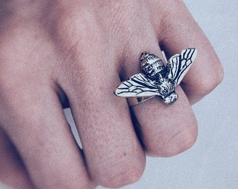 Puede incluir: Un anillo de plata con un diseño de abeja detallado con las alas extendidas. El anillo se lleva en un dedo.