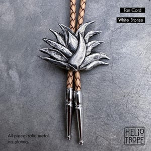 May include: A bolo tie featuring a white bronze succulent-shaped centerpiece on a tan braided cord. The cord ends are finished with polished white bronze tips. Text on the image reads: Tan Cord, White Bronze, All pieces solid metal, no plating.