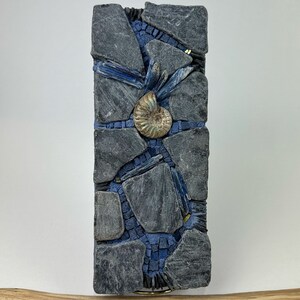May include: A mosaic wall art piece featuring a blue and gray color scheme. The mosaic is made of small pieces of slate and features a fossilized ammonite in the center.