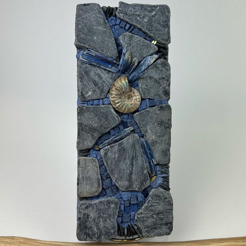 May include: A mosaic wall art piece featuring a blue and gray color scheme. The mosaic is made of small pieces of slate and features a fossilized ammonite in the center.