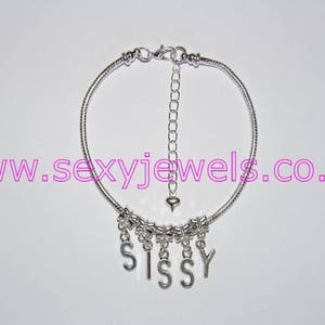 Puede incluir: Un brazalete de cadena de plata con un dije de corazón y un dije colgante que deletrea "SISSY".