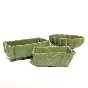 May include: Three green ceramic planters, one rectangular with a wavy edge, one rectangular with a leaf design, and one bowl-shaped with a scalloped edge.