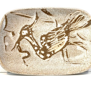 May include: A rectangular ceramic dish with a brown and white speckled glaze. A stylized bird design is painted in brown on the dish.