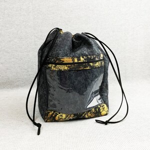 May include: A black drawstring bag with a gold and black patterned design. The bag has a clear plastic window on the front.
