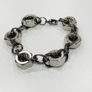 May include: A silver bracelet made of linked metal nuts. The bracelet has a clasp closure.