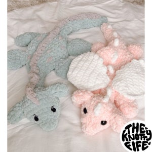 Puede incluir: Dos peluches de dragón de crochet, uno en azul claro y rosa, el otro en rosa y blanco. Los peluches están tumbados sobre una superficie blanca. El texto "PDF Pippa the Dragon Pattern" está en el lado izquierdo de la imagen y "© 2024 The Knotty Fife" está en el lado derecho de la imagen.