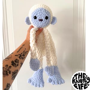 Op de afbeelding: Een handgemaakte, pluche yeti-pop in zacht, getextureerd garen. De yeti heeft een witte body, lichtblauwe kop, oren en voeten en zwarte ogen. De pop wordt door een hand omhoog gehouden. Tekst links luidt "PDF Bramble Bigfoot/Yeti Pattern".