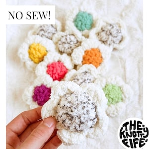 May include: A set of crocheted flower shapes in various colors, including white, pink, purple, orange, yellow, and green. The flowers are arranged in a circle on a white surface. The text "NO SEW!" is visible in the image.