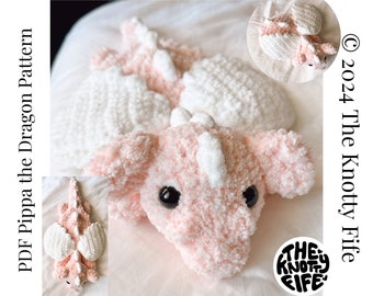 May include: A pink crocheted dragon with white wings. The dragon is lying on its side with its head resting on the ground. The dragon has black eyes and a white nose. The dragon is made with a fluffy yarn. The text "The Knotty Life" is visible in the lower right corner of the image.