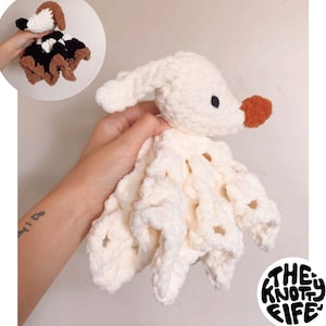 May include: A white crocheted ghost dog lovey with a brown nose and a white crocheted body. The lovey is being held by a hand with a tattoo on the wrist. The text "The Knotty Life" is visible in the bottom right corner of the image.
