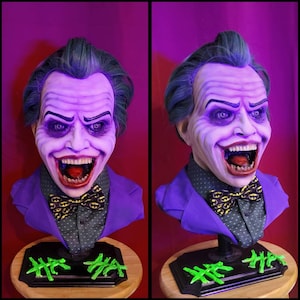Peut inclure: Buste détaillé du Joker, avec une peau violette, des cheveux verts et un large sourire menaçant. Il porte une veste de costume violette, une chemise à pois et un nœud papillon avec le logo Batman. Le buste repose sur une base en bois.