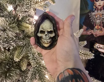 Op de afbeelding: Een zwart-witte schedelversiering met een kap, hangend aan een kerstboom.