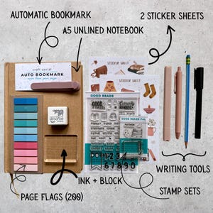 May include: A stationery set including an A5 unlined notebook, an automatic bookmark, two sticker sheets, page flags, an ink pad with a clear block, two stamp sets, and four writing tools. The items are arranged on a surface with labels.