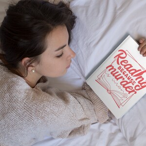May include: A white book with the text "Reading because murder is wrong" in red lettering. The book is open and a stylized illustration of a book is visible. The book is held by a person lying in bed.