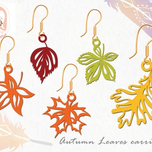 Puede incluir: Cinco pares de pendientes colgantes con diferentes diseños de hojas de otoño. Las hojas están cortadas en papel dorado, naranja, rojo y amarillo. Los pendientes están etiquetados como "Pendientes de hojas de otoño".