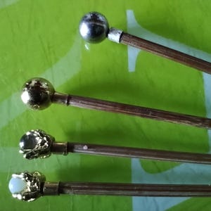 May include: Four wooden dowels with different decorative metal tops. The tops include a silver ball, a gold ball, a gold crown with a white stone, and a gold crown with a clear stone.