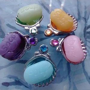 May include: Five small seashell-shaped soap dishes with colorful soap bars inside. Each dish has a jeweled accent and the word "Soap" is printed on each soap bar.