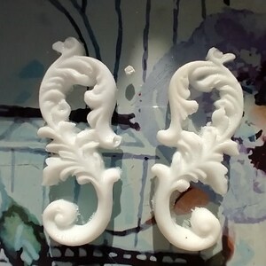 May include: Two white decorative pieces with a floral design. The pieces are made of a smooth, white material and have a delicate, intricate design.