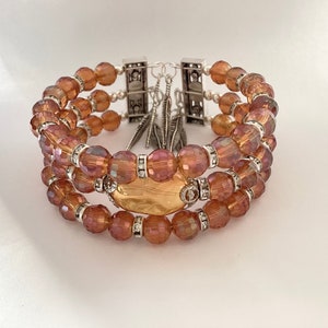 May include: A multi-strand bracelet with iridescent brown beads and a gold-toned charm. The bracelet has silver-toned clasps and feather accents.