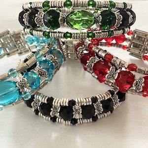 May include: Four beaded bracelets with silver accents. The bracelets are layered in a stack and feature different colored beads, including black, green, red, and blue.