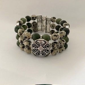 May include: A triple-strand bracelet with green and white speckled beads and a silver filigree charm. The bracelet has a silver clasp.